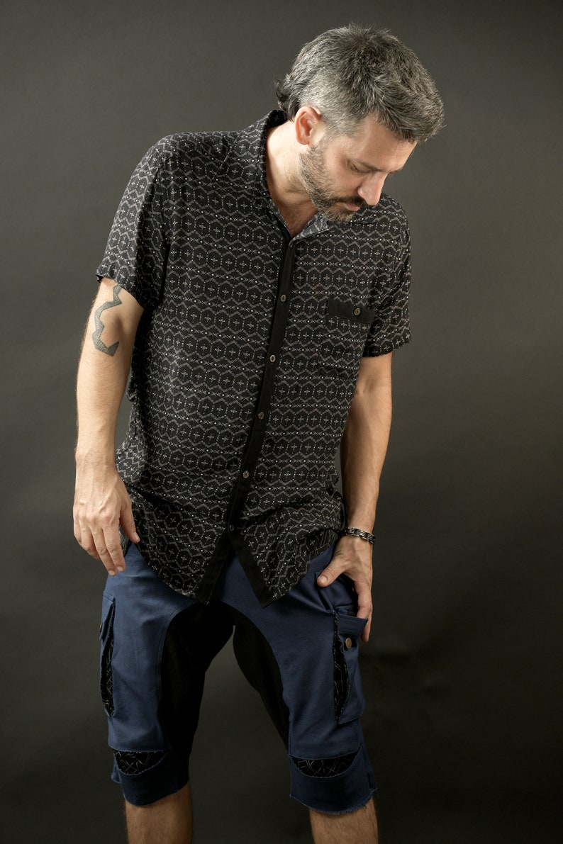 May include: A man wearing a black and white patterned short-sleeved shirt and blue denim shorts with black accents. The shorts have a large cargo pocket on the right side.