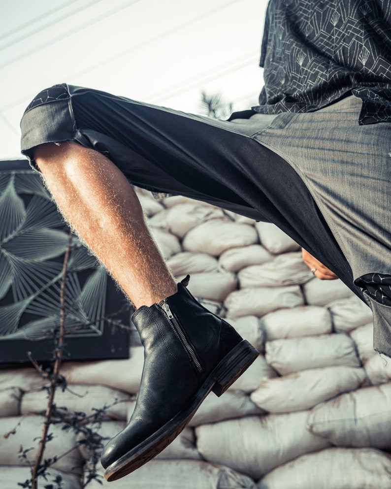 May include: A black leather ankle boot featuring a side zipper closure, a rounded toe, and a low stacked heel. The boot is constructed with smooth leather panels and a visible vertical metal zipper on the outer side, extending from the ankle collar.