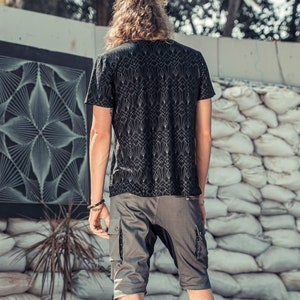 May include: A black short-sleeved t-shirt featuring a repeating white geometric art deco pattern paired with grey cargo shorts that have side pockets and dark fabric panels. The t-shirt has a crew neckline and the shorts reach above the knees.