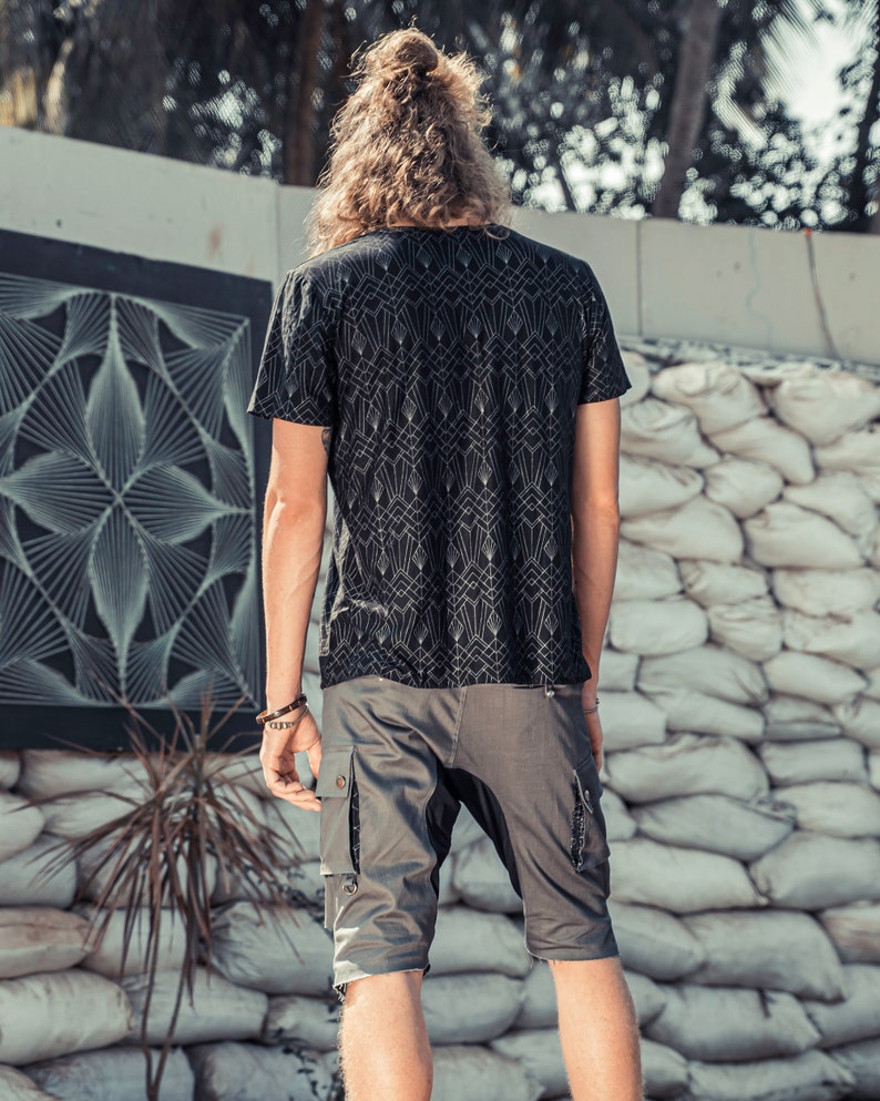 May include: A black short-sleeved t-shirt featuring a repeating white geometric art deco pattern paired with grey cargo shorts that have side pockets and dark fabric panels. The t-shirt has a crew neckline and the shorts reach above the knees.