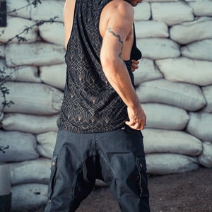 May include: A person wearing a black tank top with a gold geometric pattern and black cargo shorts. The tank top has a scoop neck and the shorts have multiple pockets.