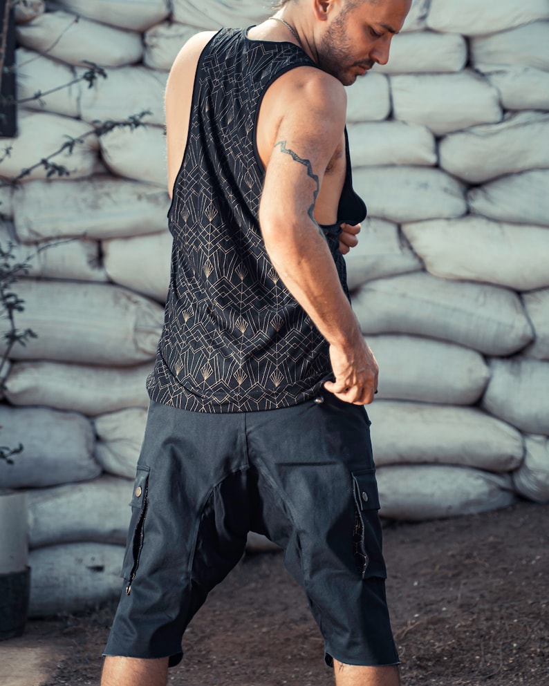 May include: A person wearing a black tank top with a gold geometric pattern and black cargo shorts. The tank top has a scoop neck and the shorts have multiple pockets.