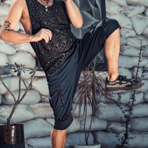 May include: A black sleeveless tank top featuring a geometric gold-toned pattern paired with black cargo-style shorts that have side pockets and dark sneakers with brown accents. The outfit is worn by a person in a dynamic pose with one leg raised.