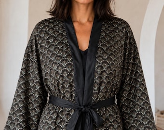 May include: A black kimono robe featuring a repeating fan-shaped pattern in gold and white. The garment has wide sleeves, a solid black satin-finish trim along the front opening, and a matching black fabric tie belt at the waist.