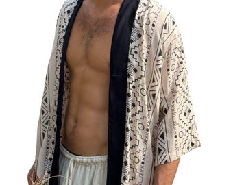 Op de afbeelding: Crèmekleurige kimono met een zwart geometrisch patroon en zwarte bies. Het open ontwerp heeft een verscheidenheid aan vormen, waaronder driehoeken, zigzags en cirkels. De mouwen zijn wijd en de stof lijkt licht.