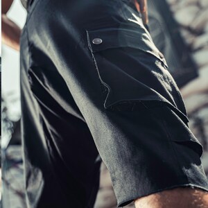 May include: Black cargo shorts with a large pocket on the right leg. The pocket has a flap with a button closure.