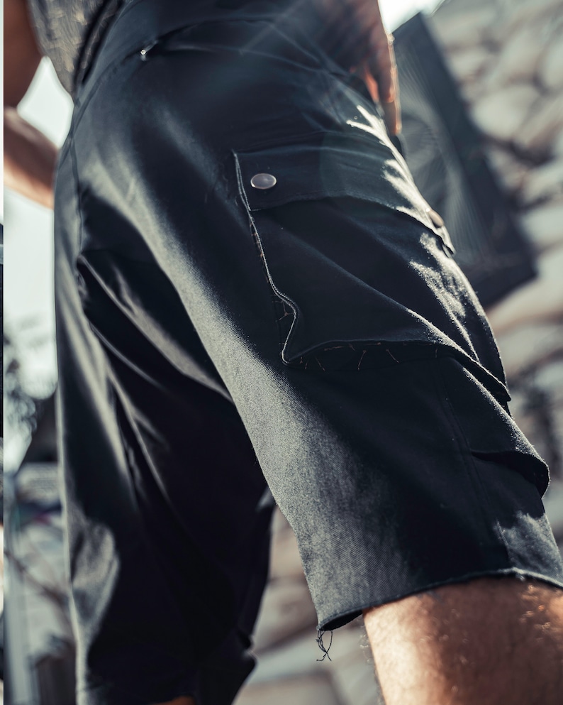 May include: Black cargo shorts with a large pocket on the right leg. The pocket has a flap with a button closure.