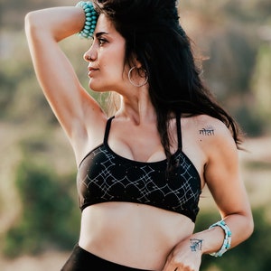 Peut inclure: Une femme portant un soutien-gorge de sport noir &agrave; motif g&eacute;om&eacute;trique et un legging noir. Elle a un petit tatouage sur l'&eacute;paule qui dit "माता" en hindi. Elle porte des bracelets turquoise aux deux poignets.