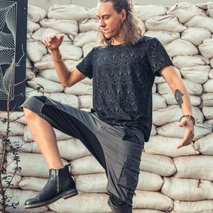 May include: A black short-sleeved t-shirt featuring a white geometric art deco pattern paired with grey cargo shorts that have black patterned pocket accents and a single black leather ankle boot with a side zipper closure.