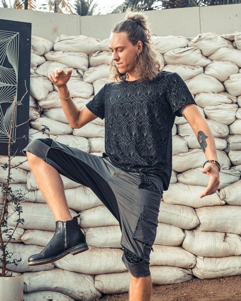 May include: A black short-sleeved t-shirt featuring a white geometric art deco pattern paired with grey cargo shorts that have black patterned pocket accents and a single black leather ankle boot with a side zipper closure.