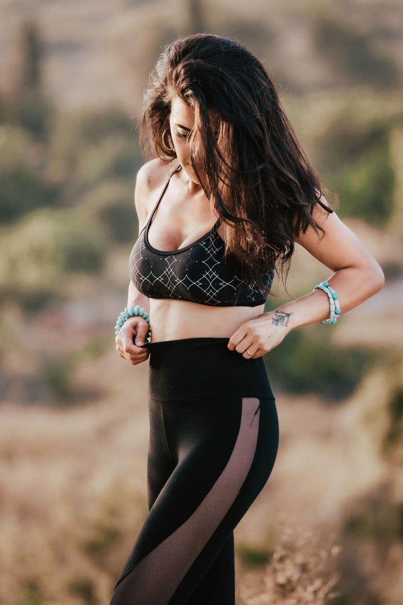 Peut inclure: Une femme portant un soutien-gorge de sport noir avec un motif g&eacute;om&eacute;trique blanc et un legging noir avec un panneau transparent sur le c&ocirc;t&eacute;. Elle ajuste la taille de son legging.