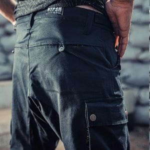 May include: Black cargo pants with a large pocket on the right leg. The pants have a belt loop and a small pocket on the back. The pants have a label that says "WTF" on the back.