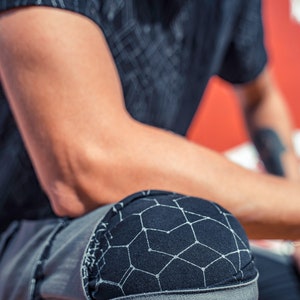 May include: A black short-sleeved shirt and grey pants featuring a black knee patch with a white geometric constellation-like pattern. The shirt also displays a matching white geometric pattern across the fabric, creating a cohesive look.