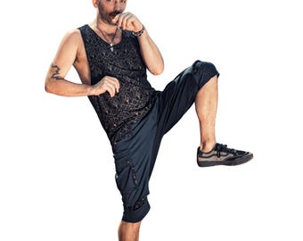 Op de afbeelding: Een zwarte tanktop met een geometrisch goudkleurig patroon en een zwarte capribroek. De outfit wordt gecombineerd met zwarte en grijze sneakers. De persoon staat in een vechtsportpositie.