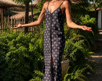 May include: A black maxi dress featuring a white geometric diamond pattern, thin spaghetti straps, and a central vertical button-down closure that runs from the V-neckline down to the hem, creating a front slit effect in the fabric.