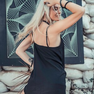 May include: A woman wearing a black slip dress with thin straps. She has long blonde hair and is wearing a black bracelet on her wrist.