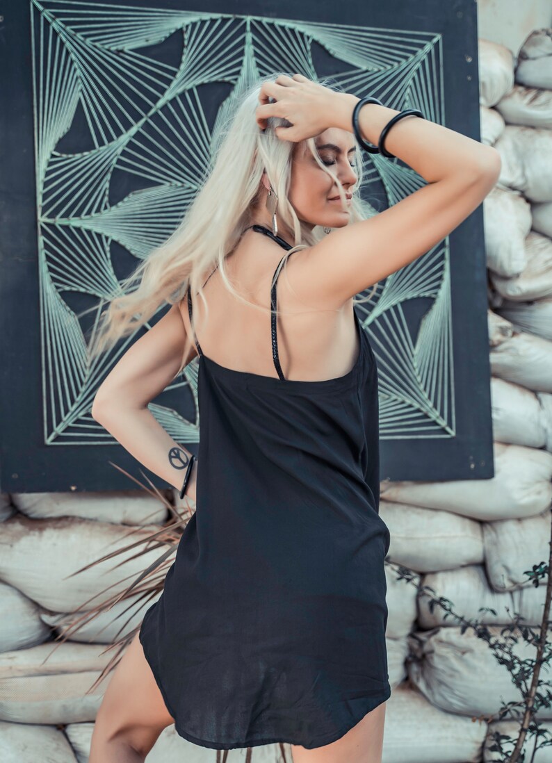 May include: A woman wearing a black slip dress with thin straps. She has long blonde hair and is wearing a black bracelet on her wrist.