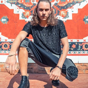 May include: A black short-sleeved t-shirt with a white geometric line pattern, paired with dark gray and black paneled shorts featuring a hexagonal print on the knees, and black leather ankle boots with side zippers and a small silver ring.