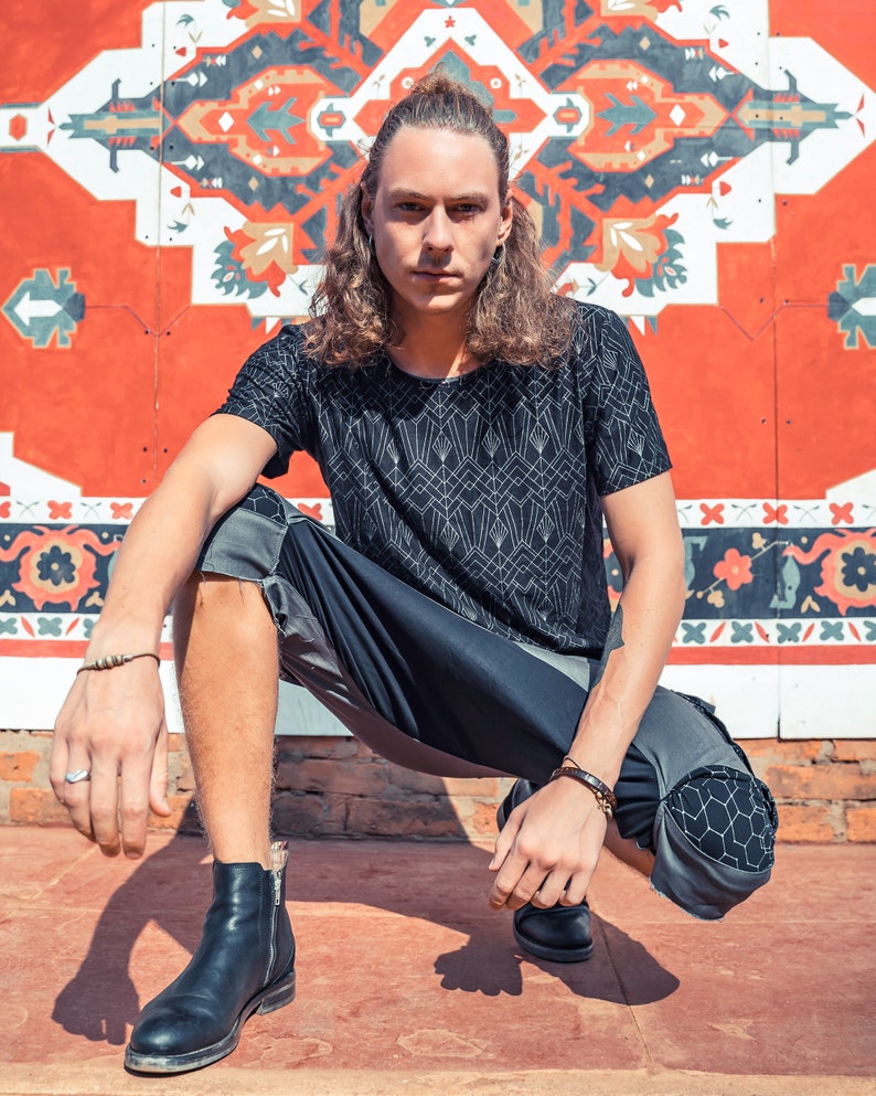 May include: A black short-sleeved t-shirt with a white geometric line pattern, paired with dark gray and black paneled shorts featuring a hexagonal print on the knees, and black leather ankle boots with side zippers and a small silver ring.