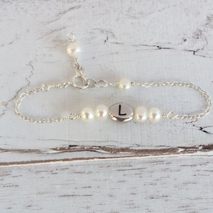 Può includere: Un braccialetto a catena d'argento con un ciondolo d'argento con la lettera "L" e perle bianche.