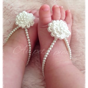 May include: White pearl anklets with a white flower accent on each foot. The flower is made of fabric and has a pearl center.