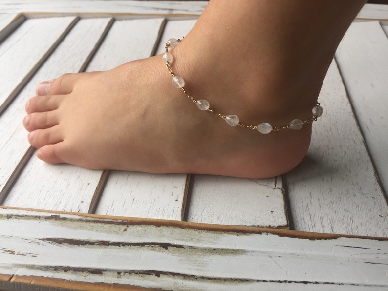 May include: A gold anklet with white moonstone beads. The anklet is on a person's ankle.