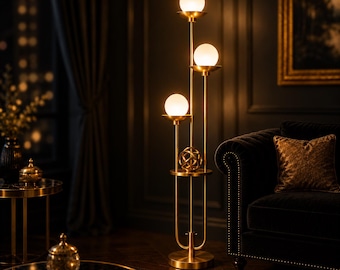 May include: A tall floor lamp with a brushed gold metal frame featuring three vertical stems of varying heights, each topped with a spherical white glass globe light. A decorative gold metal sphere sits on a circular shelf.
