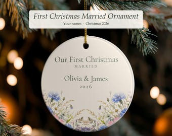 Può includere: Un addobbo natalizio rotondo in ceramica bianca con il testo Our First Christmas MARRIED, i nomi Olivia & James e l'anno 2026. La parte inferiore dell'ornamento è decorata con una colorata illustrazione botanica di fiordalisi e fiori selvatici.