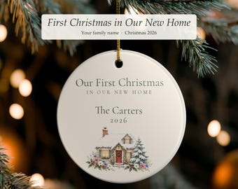 Può includere: Un ornamento rotondo in ceramica bianca con il testo Our First Christmas IN OUR NEW HOME, The Carters e 2026. Sotto il testo si trova un'illustrazione colorata di una casa coperta di neve con una porta rossa, un camino e un pino.