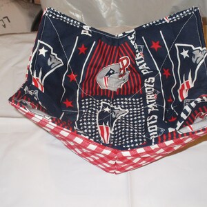 May include: A fabric bowl cozy featuring a navy blue and red Patriots design with stars and the team logo. The bottom edge is red and white gingham. This item is designed to be microwave safe.