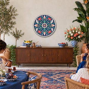 May include: A circular wall plate featuring a symmetrical floral pattern with red, white, and blue colors. The design includes stylized tulips and intricate foliage on a deep blue background, mounted on a plain wall above a wooden sideboard.