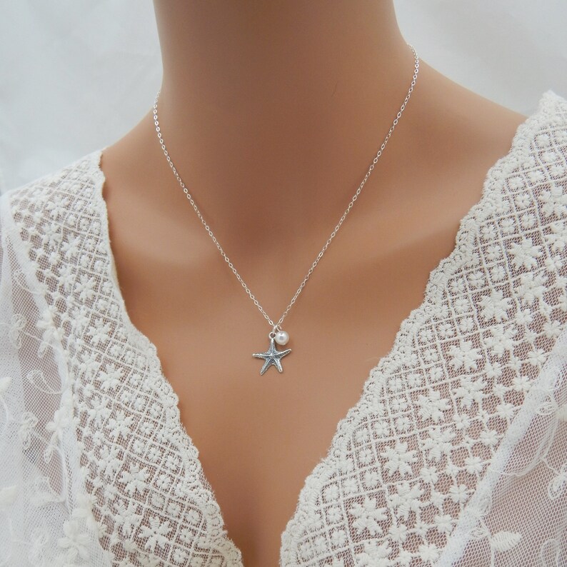 Puede incluir: Un collar de cadena de plata con un peque&ntilde;o dije de perla y un dije de estrella de mar de plata.