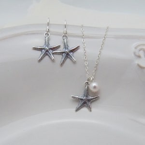 Puede incluir: Un conjunto de collar y pendientes de plata con un colgante de estrella de mar con un acento de perla. El collar tiene una cadena delicada y los pendientes son de estilo colgante.