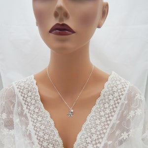 Puede incluir: Un collar de plata con un dije de estrella de mar y una perla. El collar est&aacute; en un maniqu&iacute; de encaje blanco.