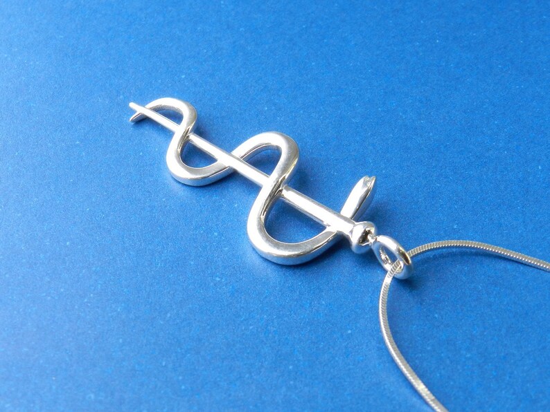 May include: A silver medical caduceus pendant necklace on a silver chain. The caduceus is a symbol of medicine and healing.