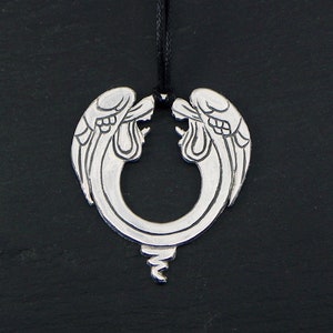 May include: A silver pendant necklace with a design of two angel wings forming a circle. The wings are detailed with etched lines and attached to a black cord. The pendant has a decorative, curled tail.