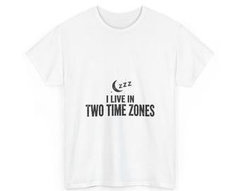May include: A white short-sleeved t-shirt featuring a black graphic of a crescent moon with ZZZ text above the words I LIVE IN TWO TIME ZONES printed in a bold, sans-serif font centered on the chest area of the garment.