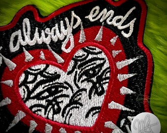 Puede incluir: Parche bordado con borde negro y centro rojo en forma de corazón. El corazón está relleno con un diseño en blanco y negro. Las palabras "always ends" están bordadas en blanco.
