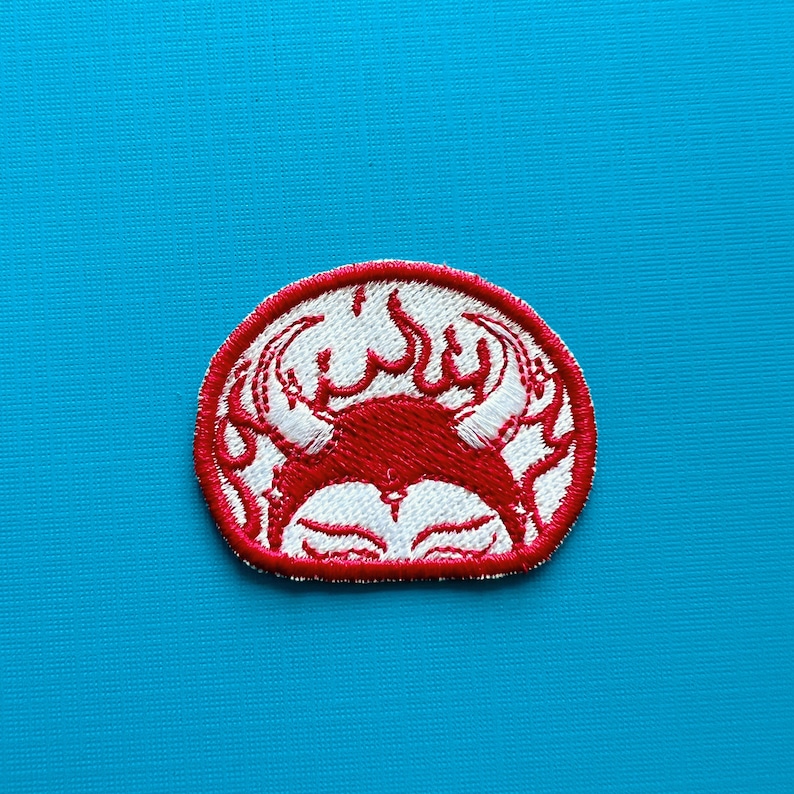 Pu&ograve; includere: Toppa ricamata con un design di granchio rosso e dettagli bianchi, su sfondo bianco all'interno di un cerchio rosso. Il granchio ha un aspetto stilizzato con fiamme. Per abbigliamento o accessori.