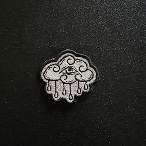May include: White embroidered patch of a cloud with an eye in the center and raindrops falling from it.