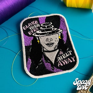 May include: Embroidered iron-on patch featuring a woman with a purple and black background. The woman has a ring of planets around her head and the text "Close Your Eyes & Melt Away".