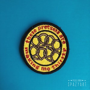 May include: A yellow and black embroidered patch with the text "These pretzels are making me thirsty" in red.