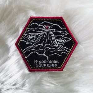 May include: Black and white embroidered patch with a red border. The patch features a stylized eye with a cross over it, surrounded by clouds. The text "If you close your eyes" is embroidered below the eye.