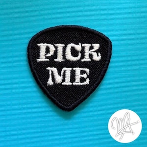 May include: Black guitar pick-shaped patch with the words "PICK ME" embroidered in white. The patch has a black border and is set against a bright blue background. A white logo is in the lower right corner.