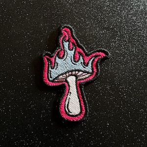 May include: A blue and pink embroidered patch of a mushroom with flames on top. The mushroom is white with a pink cap and the flames are pink.