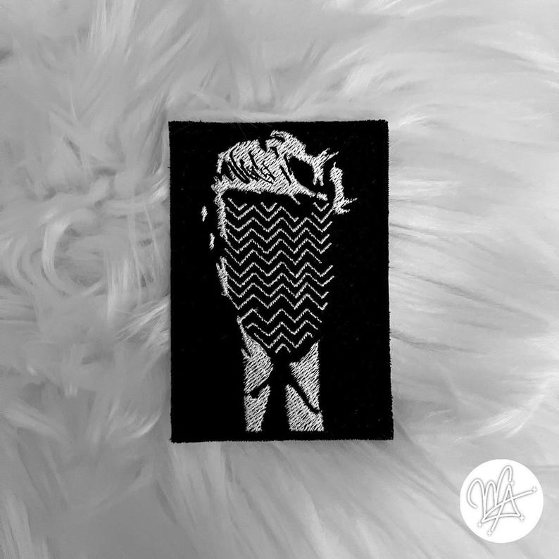 Peut inclure: Patch brod&eacute; noir et blanc repr&eacute;sentant une image stylis&eacute;e d'une t&ecirc;te humaine avec un motif en zigzag.