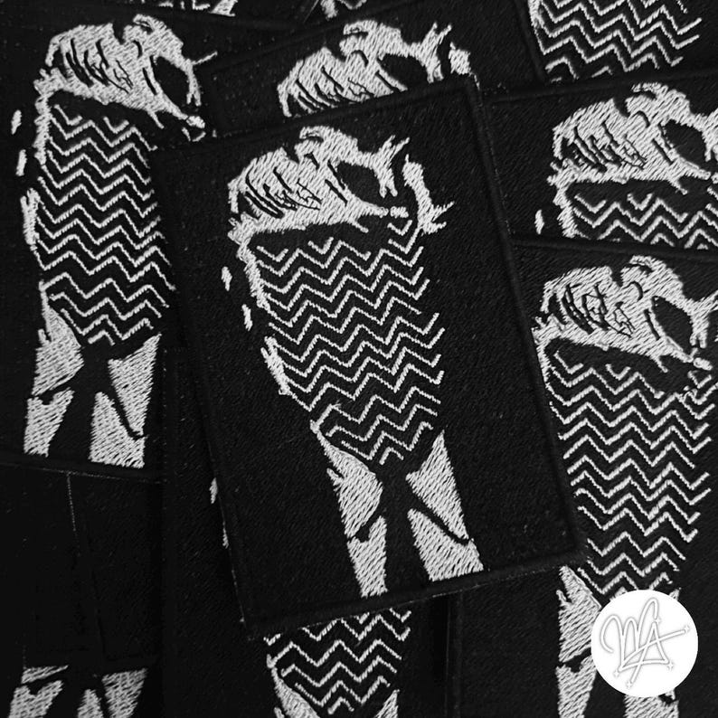 Peut inclure: Patchs thermocollants brod&eacute;s en noir et blanc repr&eacute;sentant une silhouette de personne avec un motif en zigzag.