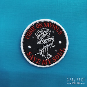 May include: A black and white embroidered patch with a white rose and dagger design. The text "Come On Saviour Save My Soul" is embroidered in red around the design.