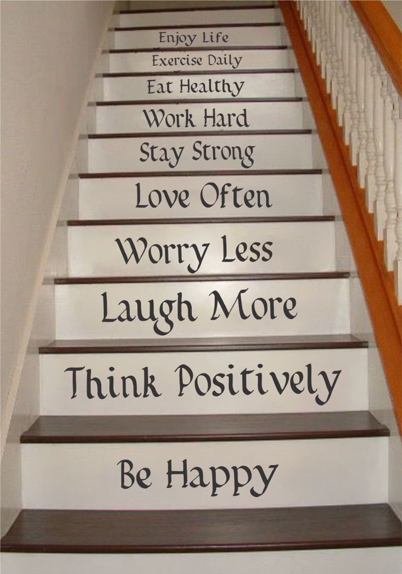 May include: A staircase with white risers featuring black text decals that read: Enjoy Life, Exercise Daily, Eat Healthy, Work Hard, Stay Strong, Love Often, Worry Less, Laugh More, Think Positively, and Be Happy, with dark brown wooden treads.