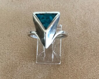 May include: A silver ring with a triangular turquoise stone set in the center. The ring has a unique, geometric design.